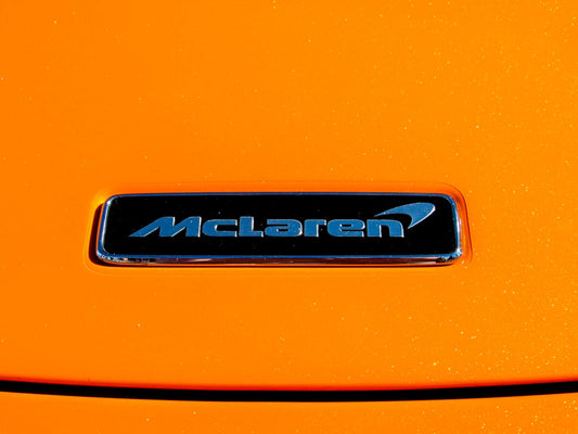 McLaren badge on vibrant orange supercar hood, close-up detail