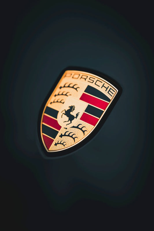 Close-up of a Porsche car emblem badge on a dark background, luxury sports car detail