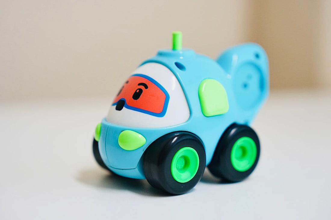 Cute blue plastic toy car with green wheels and cartoon face on white background
