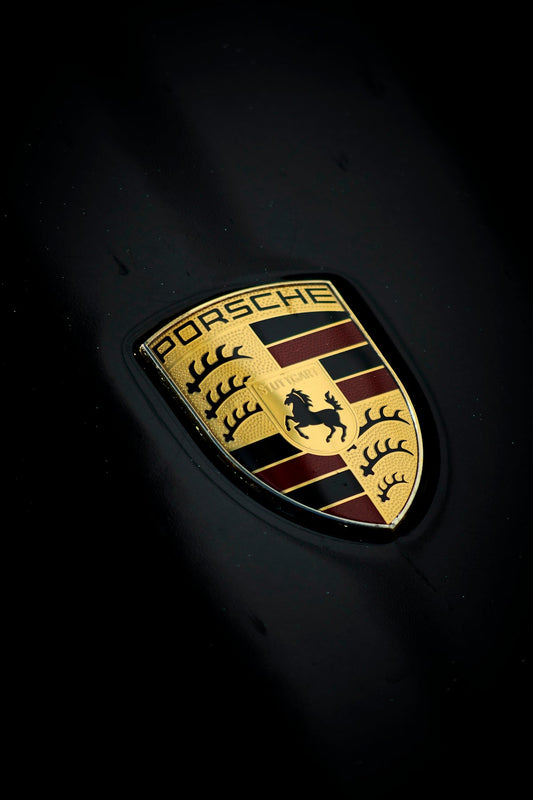 Close-up of Porsche logo emblem on a glossy black exotic sports car hood
