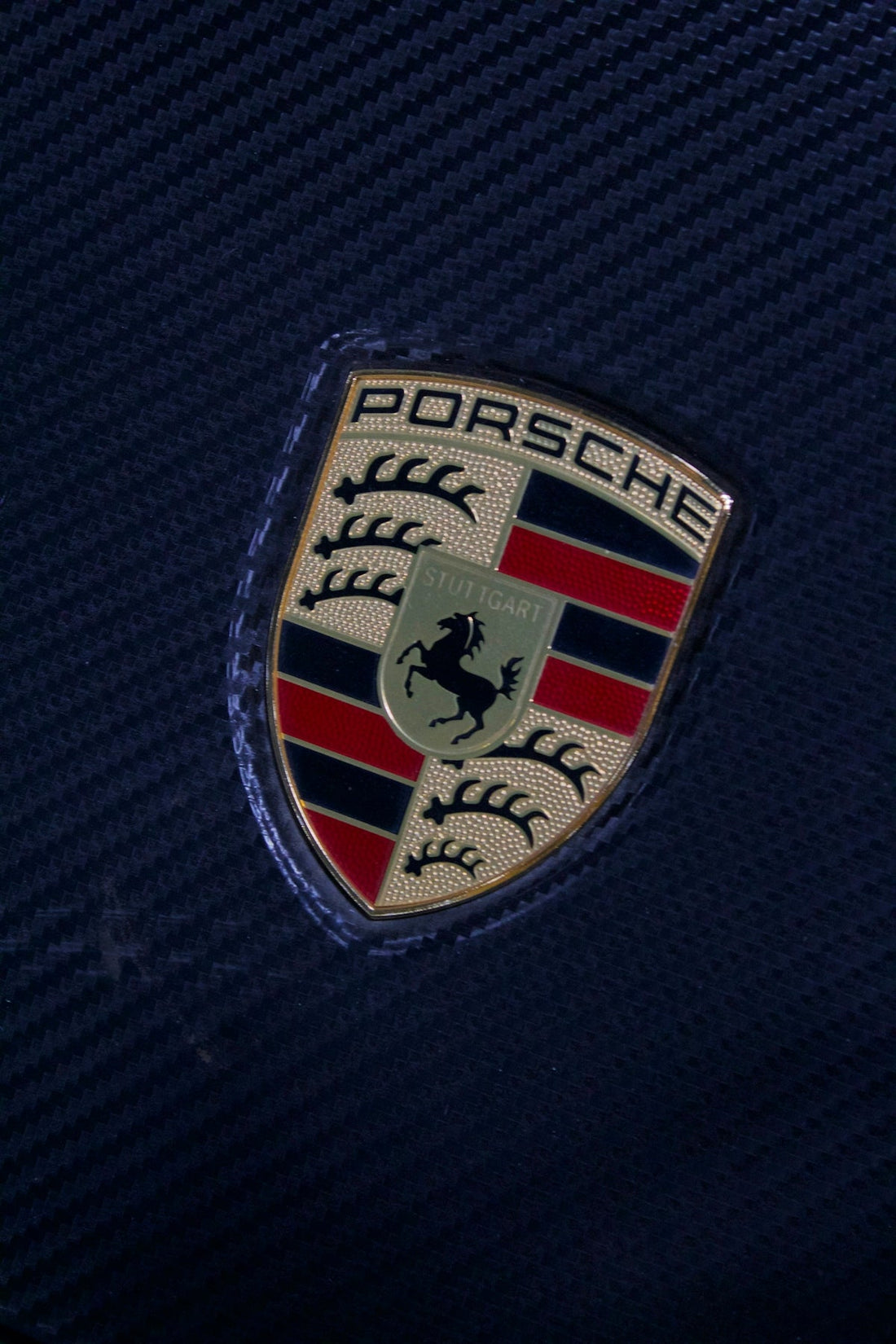 Close-up of Porsche emblem on carbon fiber panel, luxury car accessory detail