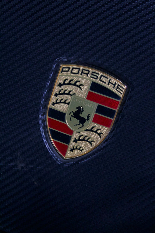 Close-up of Porsche emblem on carbon fiber panel, luxury car accessory detail