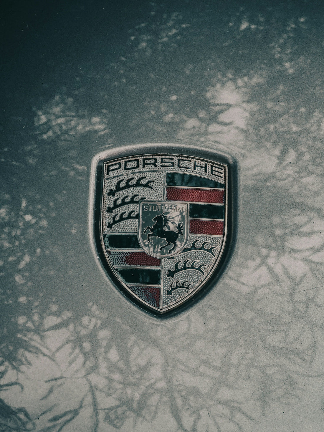 Porsche logo emblem on a silver exotic car hood with natural shadow reflections