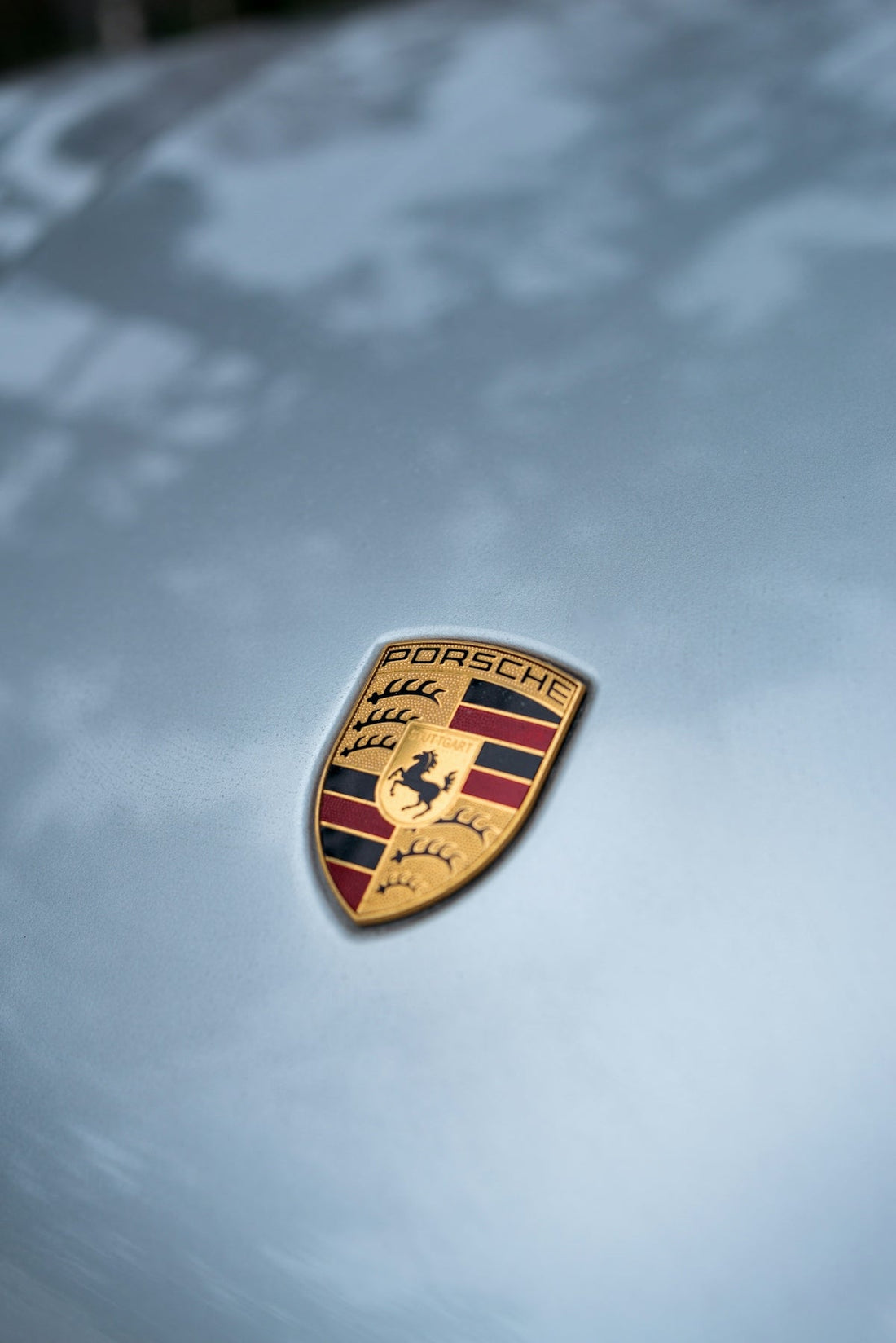 Porsche emblem on silver luxury sports car hood, clear close-up with reflections