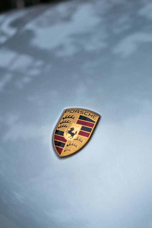 Porsche emblem on silver luxury sports car hood, clear close-up with reflections