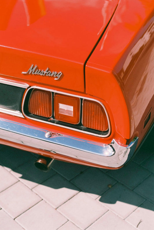 Red classic Mustang rear with chrome bumper and taillights, parked on paved surface