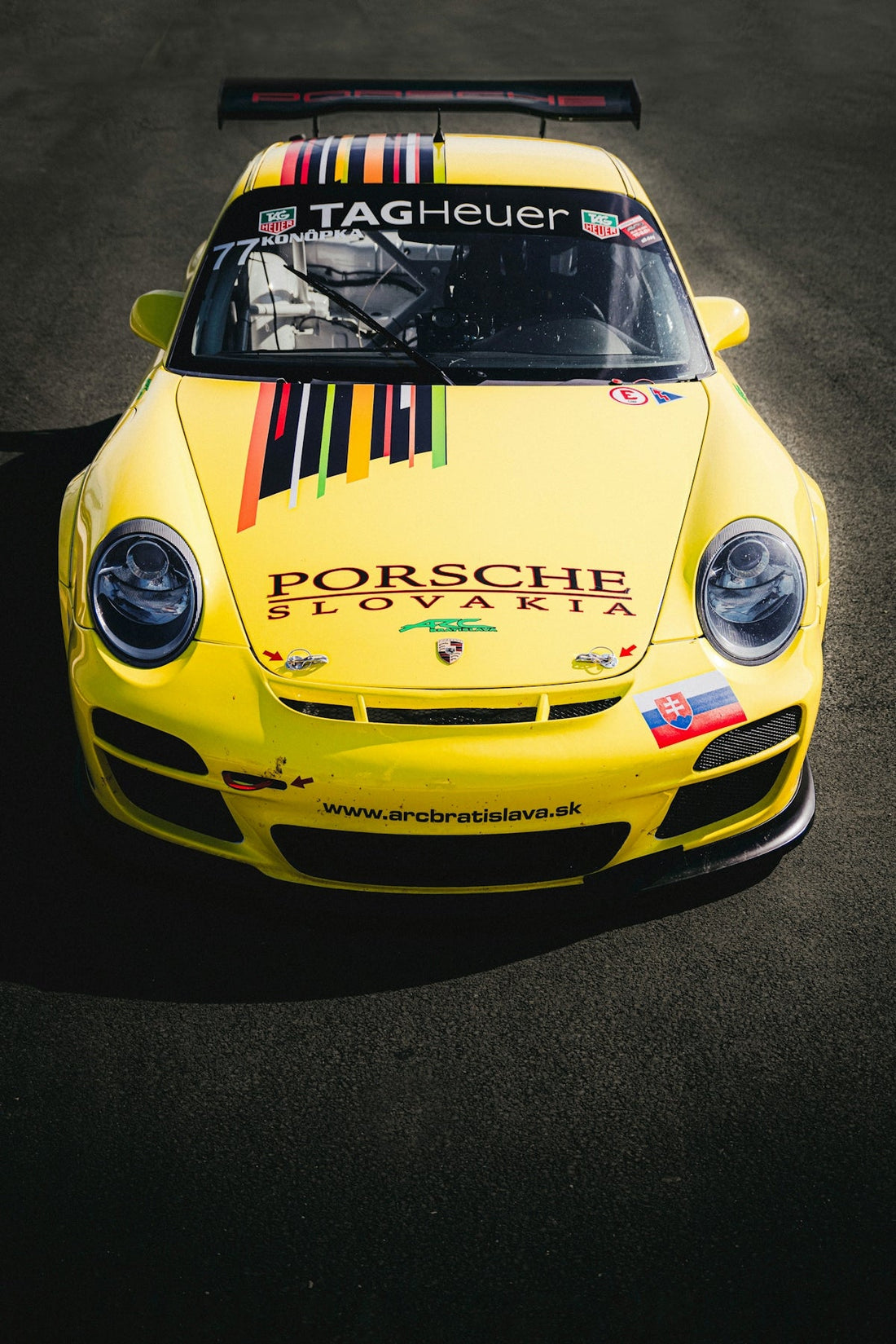 Yellow Porsche race car with Slovakia logos and colorful stripes on asphalt