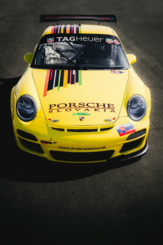 Yellow Porsche race car with Slovakia logos and colorful stripes on asphalt