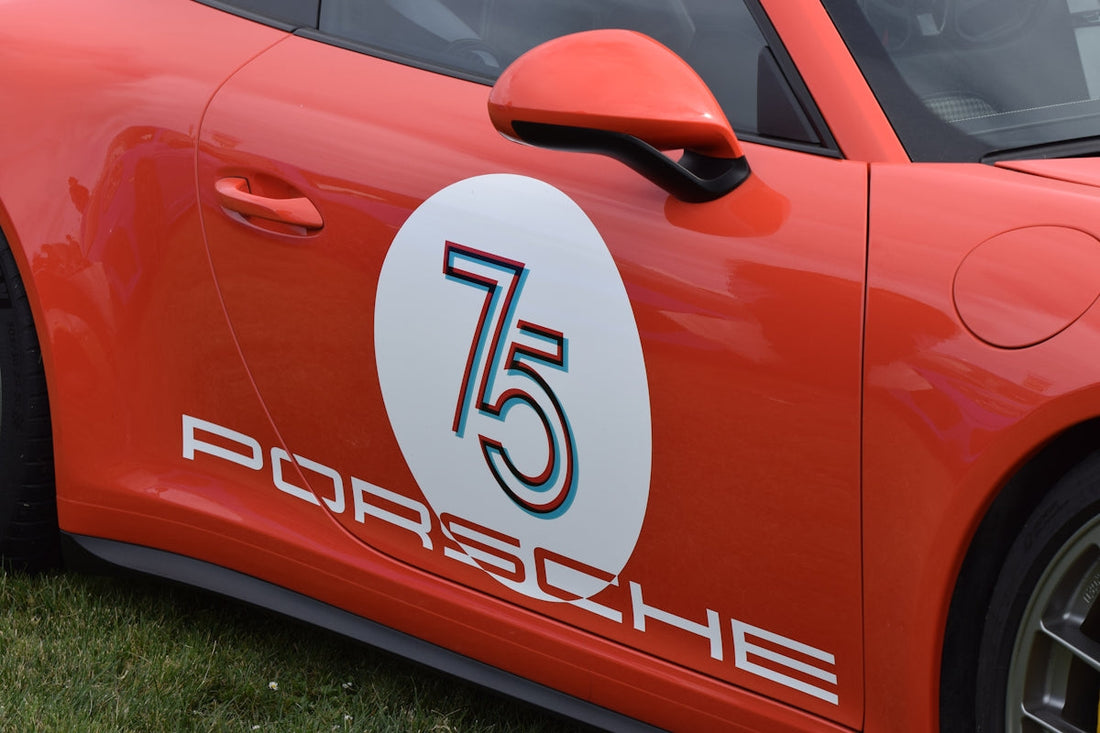 Red Porsche sports car door with 75th anniversary racing decal on grass