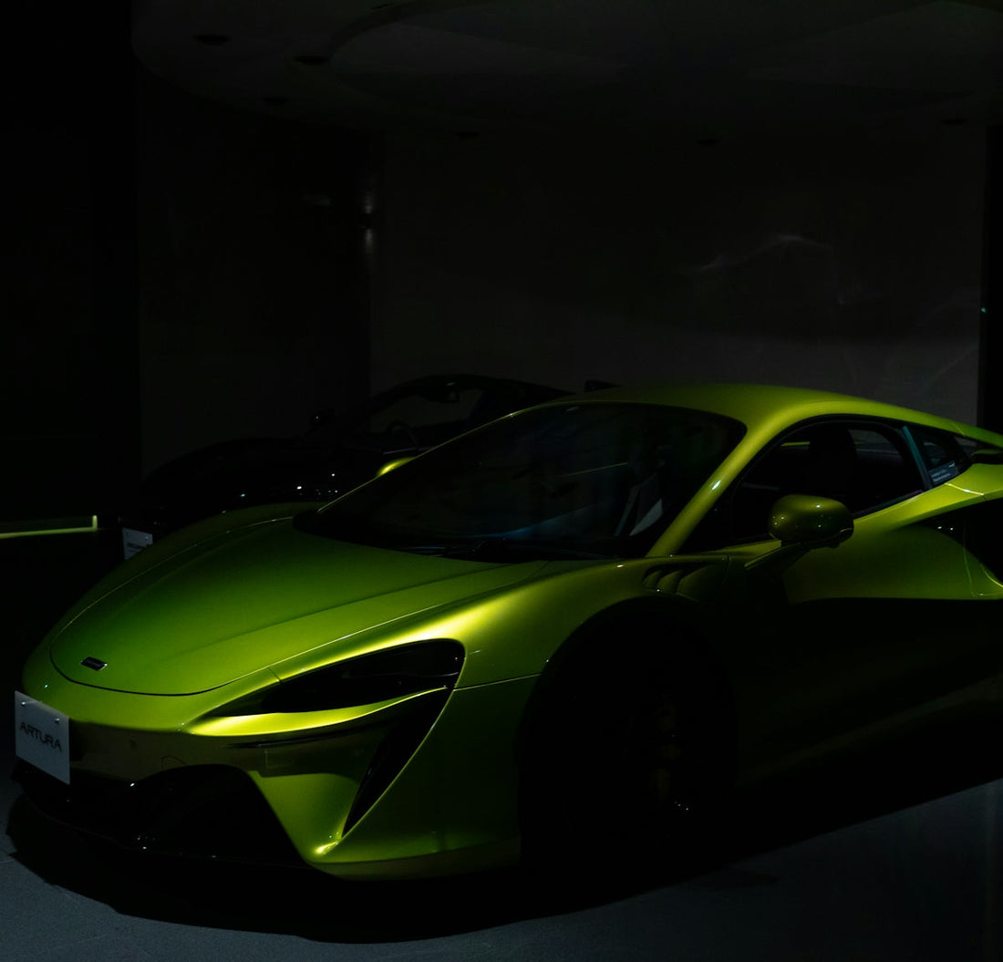 Green McLaren Artura supercar in a dimly lit showroom, highlighting its sleek design.