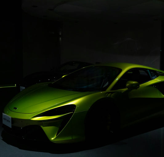 Green McLaren Artura supercar in a dimly lit showroom, highlighting its sleek design.