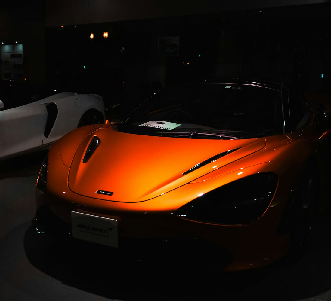 Orange McLaren supercar in showroom next to white exotic car, luxury sports vehicles display