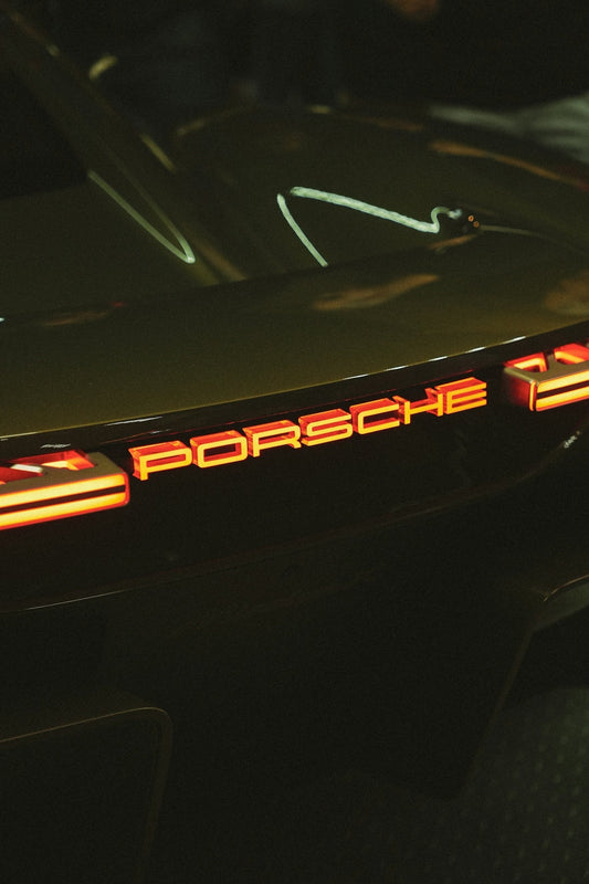 Close-up of illuminated Porsche logo on supercar rear with modern taillights at night