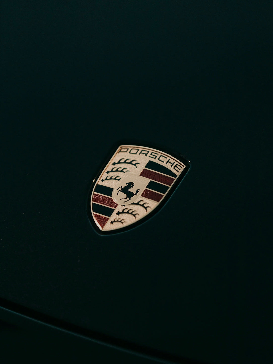 Close-up of Porsche car emblem on a dark hood, luxury sports car badge