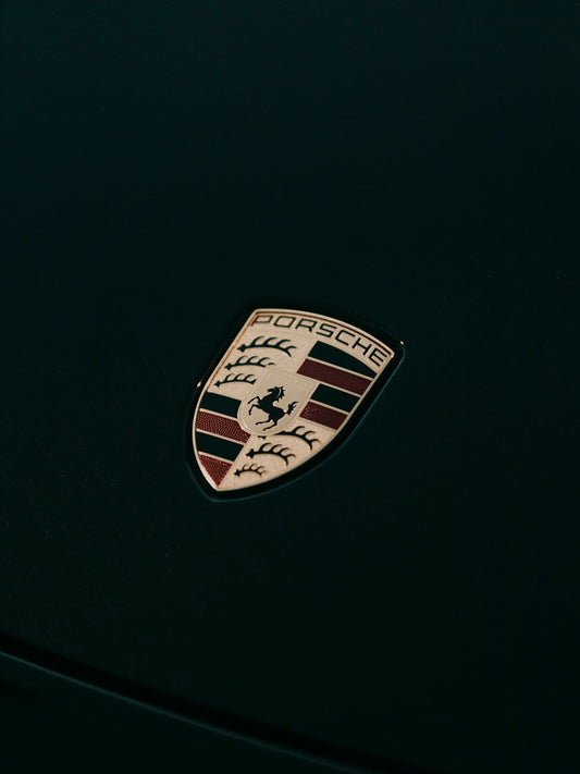 Close-up of Porsche car emblem on a dark hood, luxury sports car badge