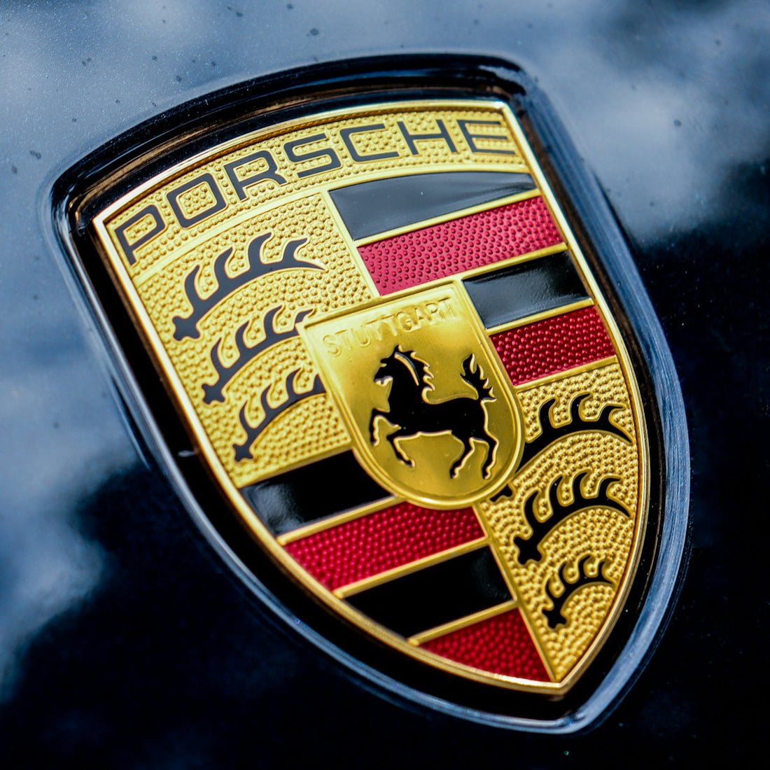 Close-up of Porsche emblem on glossy black sports car hood, high-end automotive badge