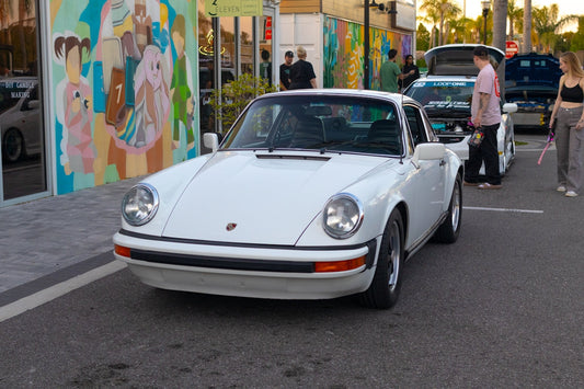 White classic Porsche sports car parked on street with mural and people nearby