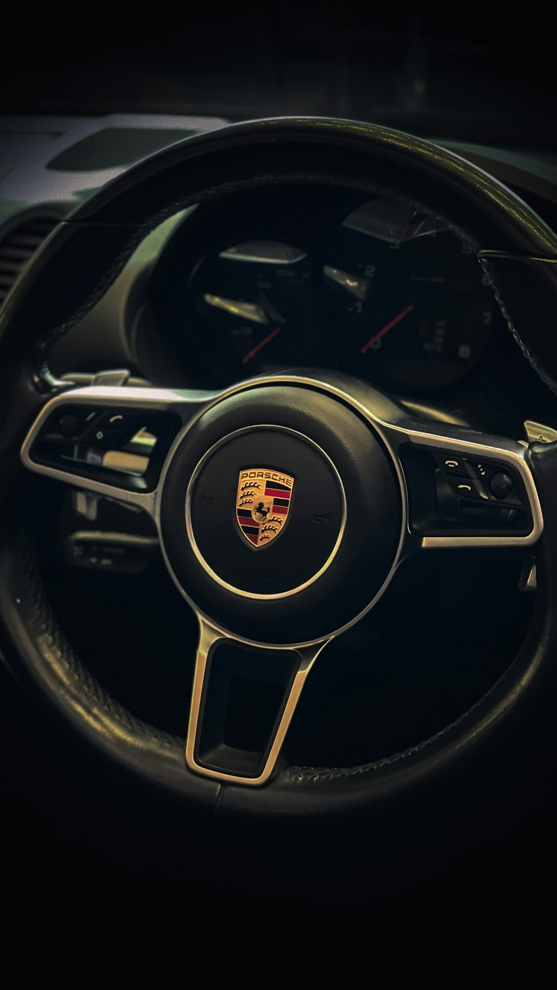 the steering wheel of a porsche car in a dark room