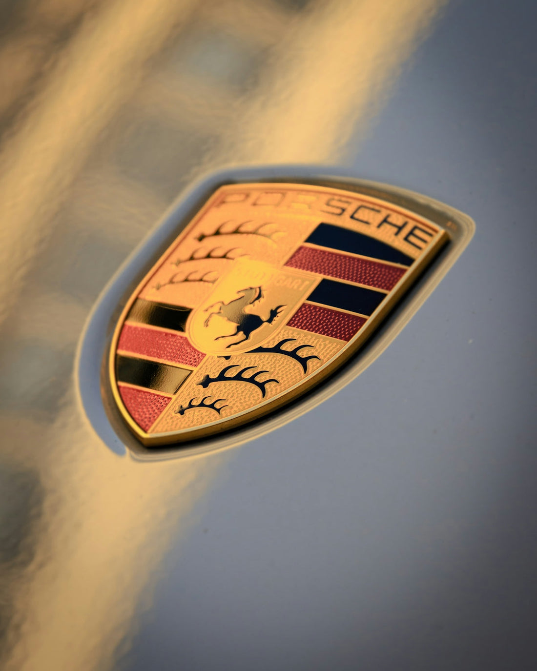 Close-up of Porsche car emblem on metallic silver hood, luxury sports vehicle detail