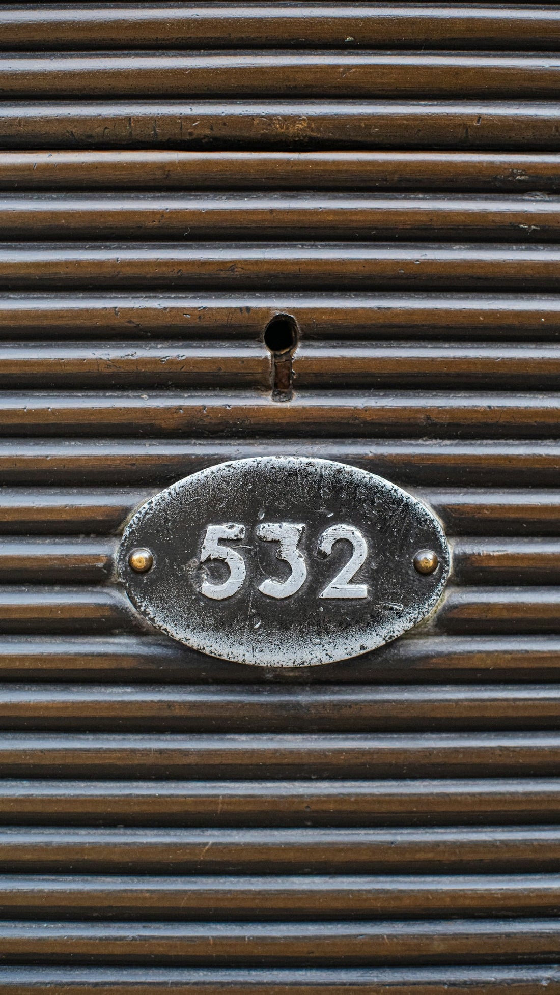 Close-up of vintage metal locker with keyhole and number 532 on ribbed brown surface