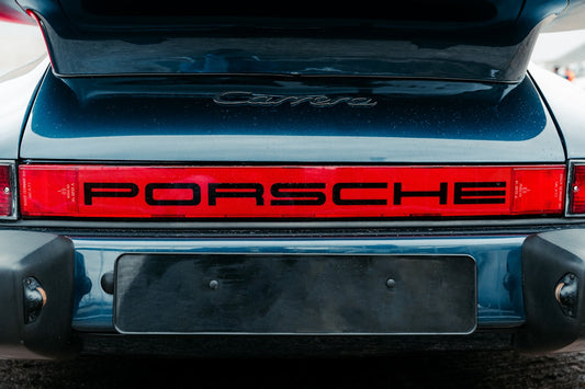 Close-up of a Porsche Carrera rear with red taillight and Porsche logo, luxury sports car