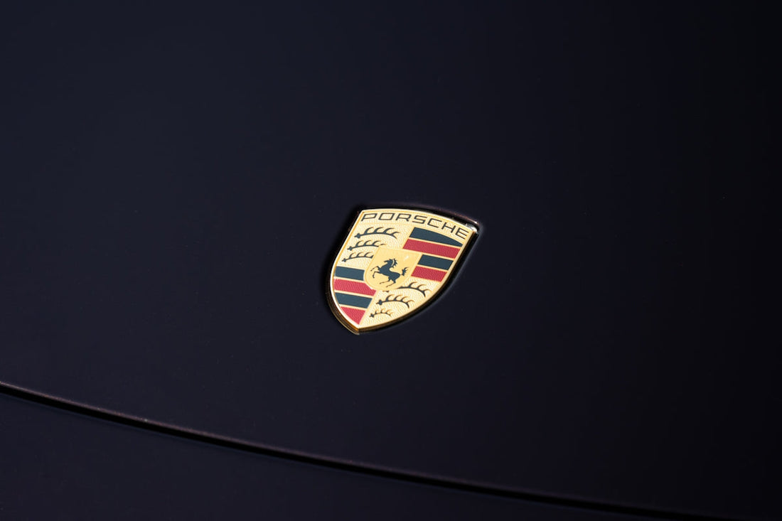 Porsche logo on dark glossy car hood, luxury exotic car detail