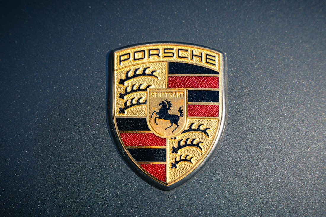 Close-up of Porsche car emblem on metallic grey exterior, luxury supercar badge