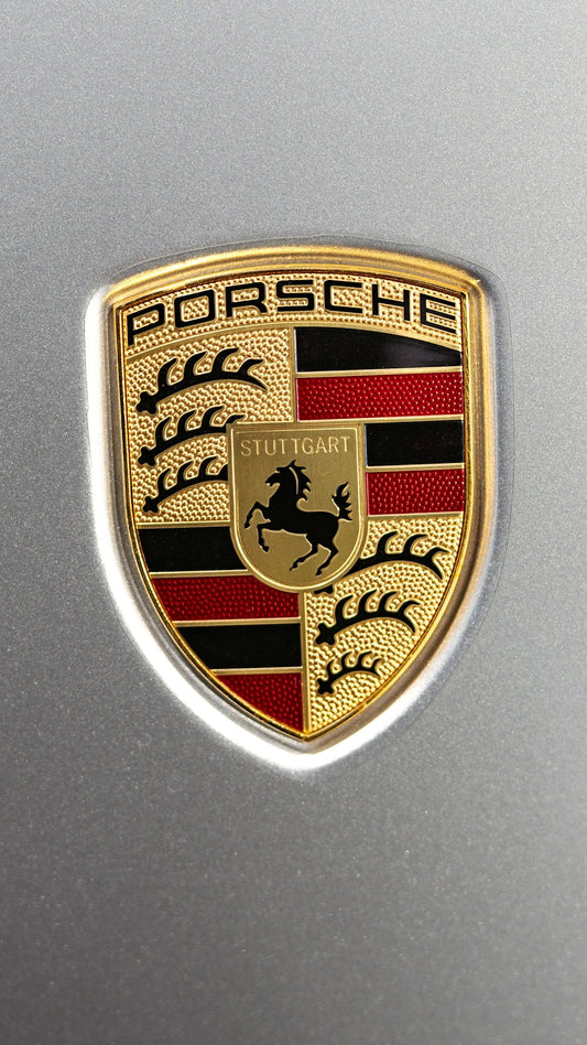 Close-up of Porsche badge on silver car hood, luxury sports car emblem