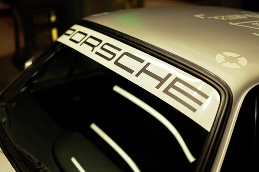 Close-up of a silver Porsche car windshield with bold Porsche decal banner.