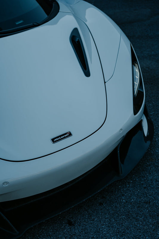 Close-up of white McLaren supercar hood, showing vent, headlight, and logo detail