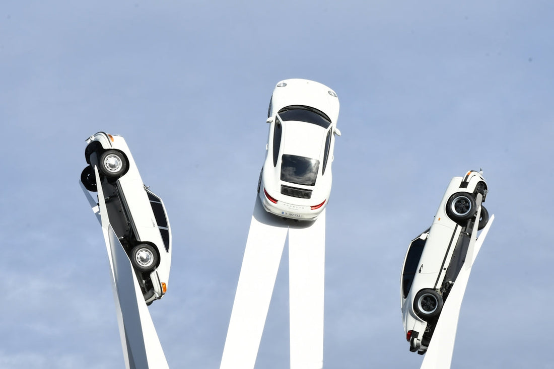 Three classic white sports cars mounted on sculptural pillars against a blue sky