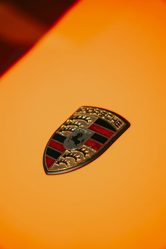 Porsche emblem on orange supercar hood, luxury exotic car detail