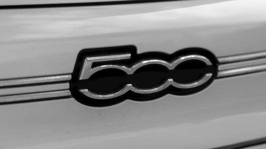 Close-up of Fiat 500 chrome badge on a white car exterior, automotive emblem detail