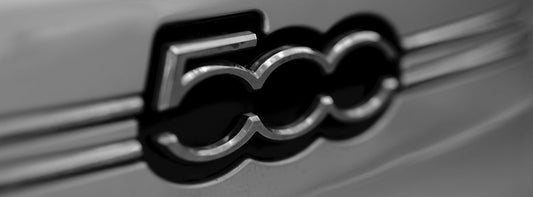 Close-up of Fiat 500 car emblem on a silver vehicle, automotive badge detail