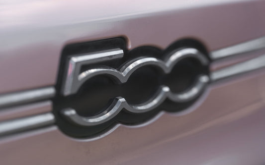 Close-up of Fiat 500 chrome badge on a pink exterior car panel