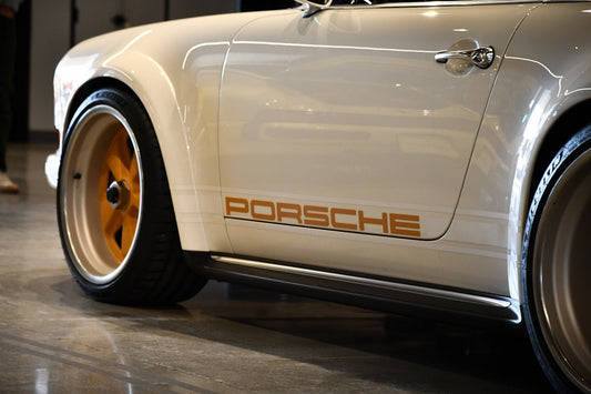 Close-up of a white Porsche sports car with gold rims and Porsche logo on the door