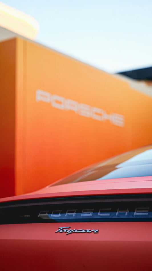 Close-up of red Porsche Taycan rear badge with orange Porsche sign background
