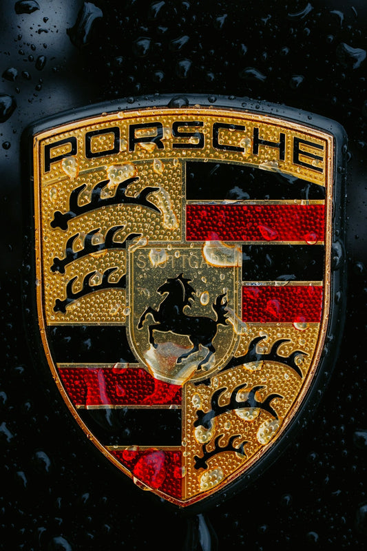 Close-up of Porsche crest emblem with water droplets on black luxury car hood