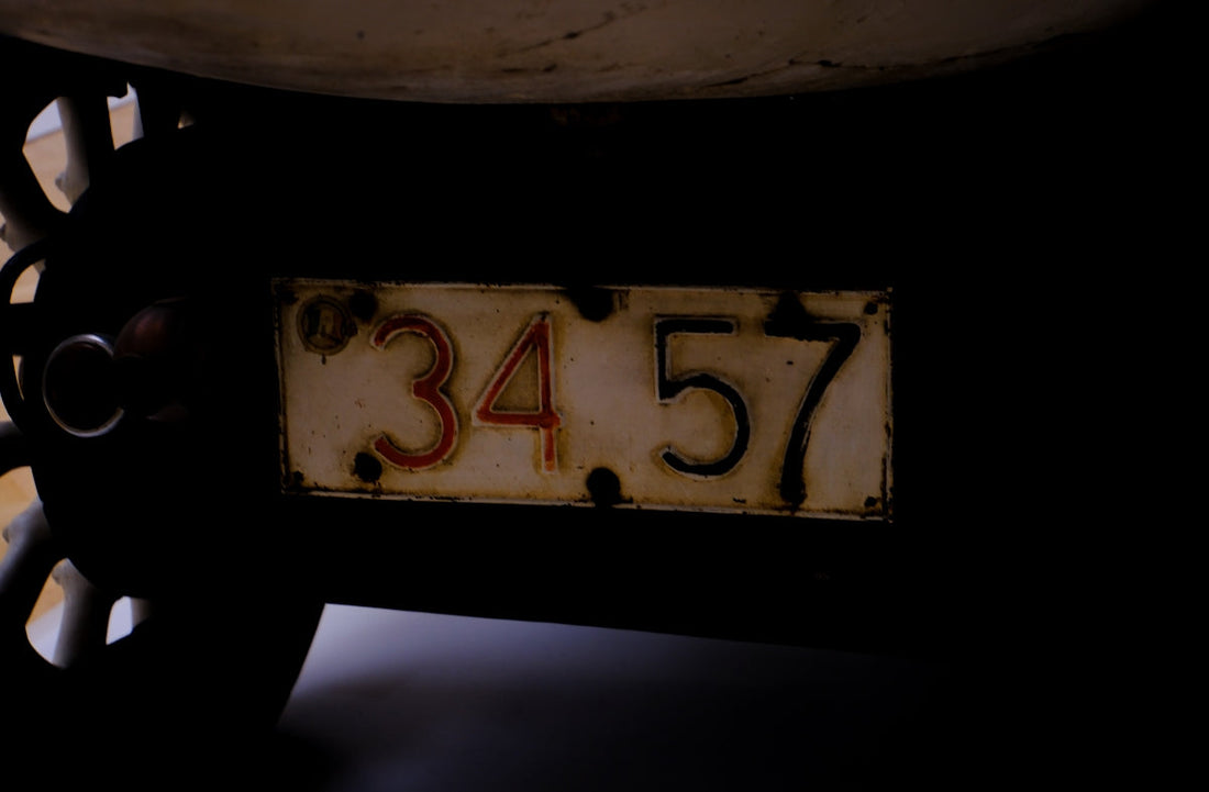 Close-up of vintage car license plate with number 3457, classic wheel visible