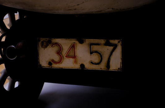 Close-up of vintage car license plate with number 3457, classic wheel visible