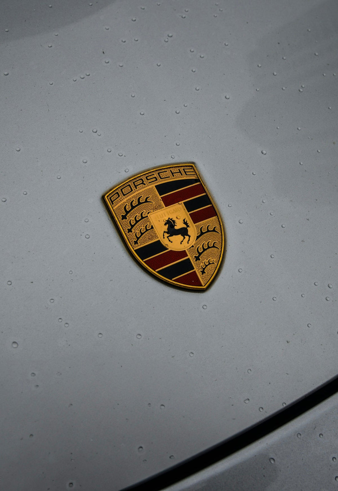 Close-up of Porsche crest emblem on grey exotic car hood with water droplets