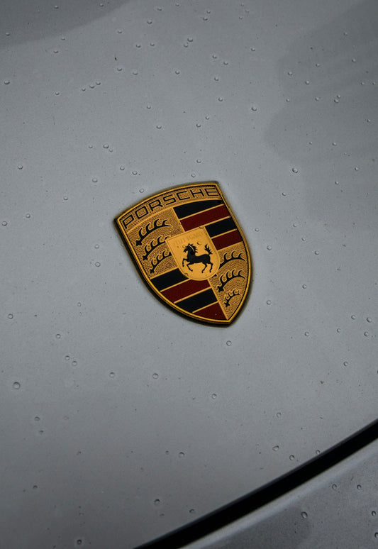 Close-up of Porsche crest emblem on grey exotic car hood with water droplets