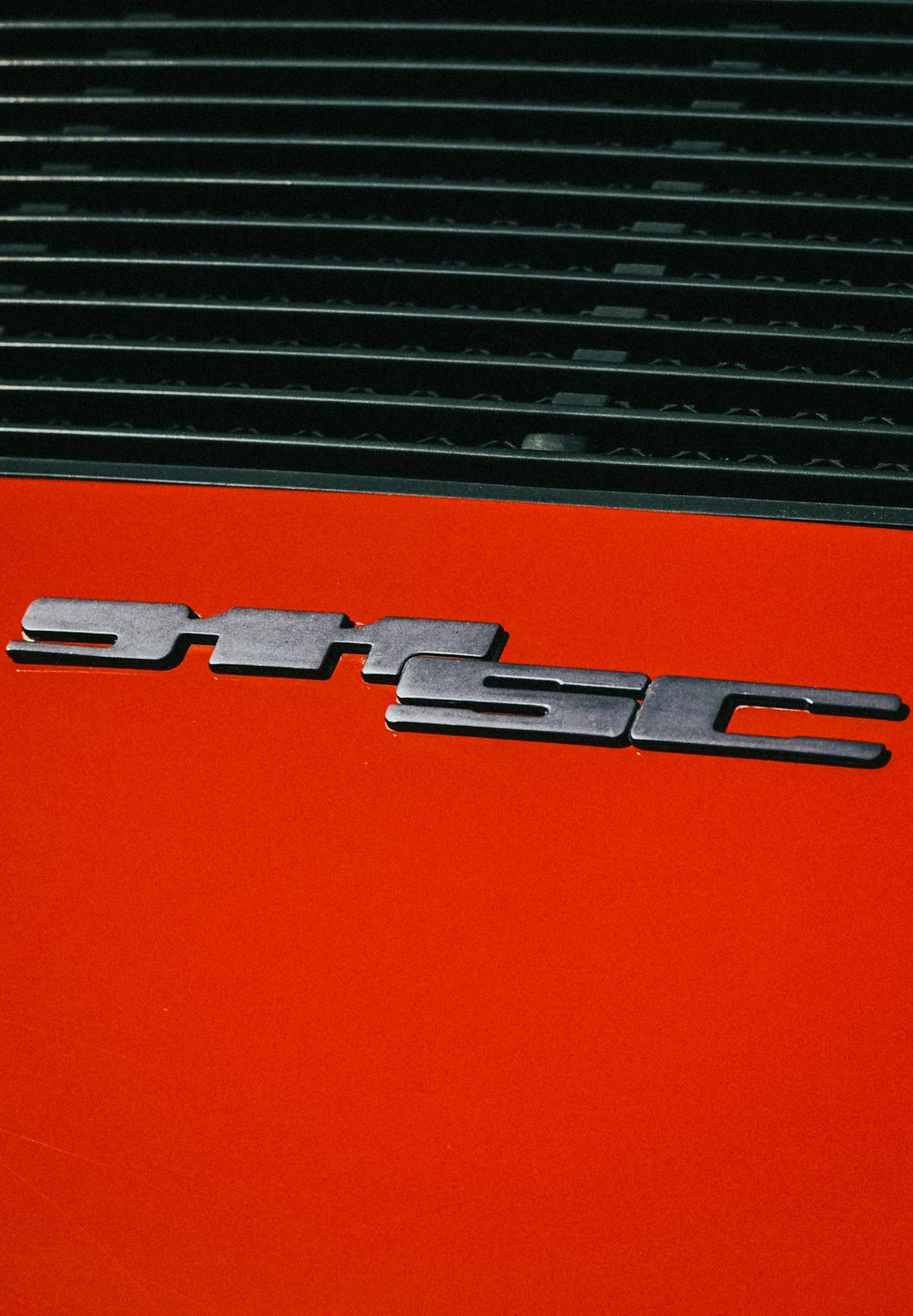 Close-up of orange Ferrari 355 GTS badge and rear air vents, exotic car detail