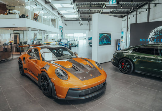 Orange Porsche 911 GT3 RS in a luxury car showroom with sports cars and modern interior
