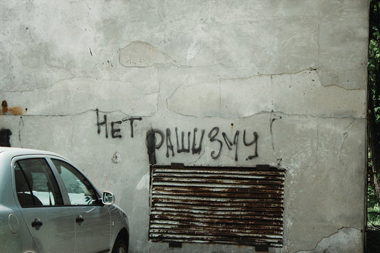 Graffiti on old concrete wall beside parked silver car, urban street scene