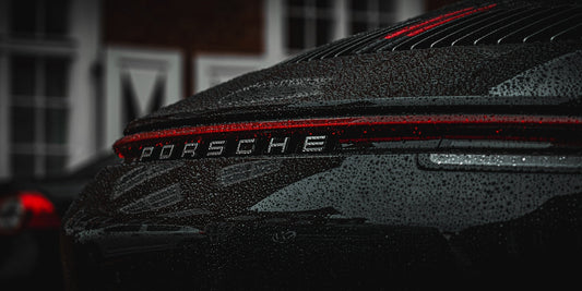 Close-up of a wet black Porsche sports car rear with raindrops and tail light