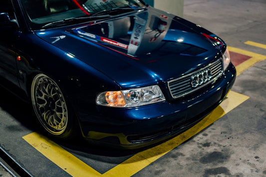 Blue Audi sedan with aftermarket wheels parked at a gas station, front end view