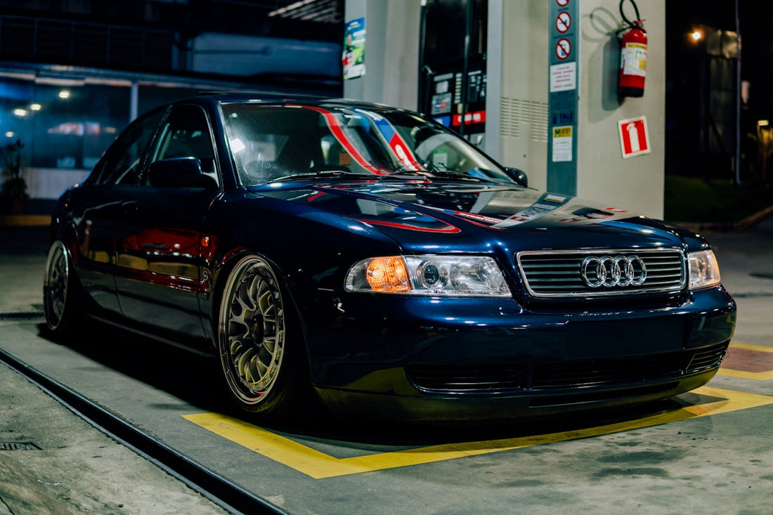 Dark blue Audi sedan with aftermarket wheels parked at night at a gas station