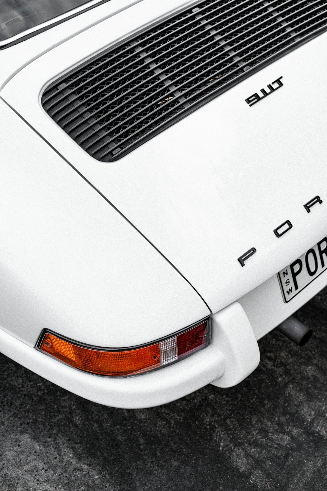 Close-up of white Porsche 911S rear, featuring tail light, air vent, and partial license plate
