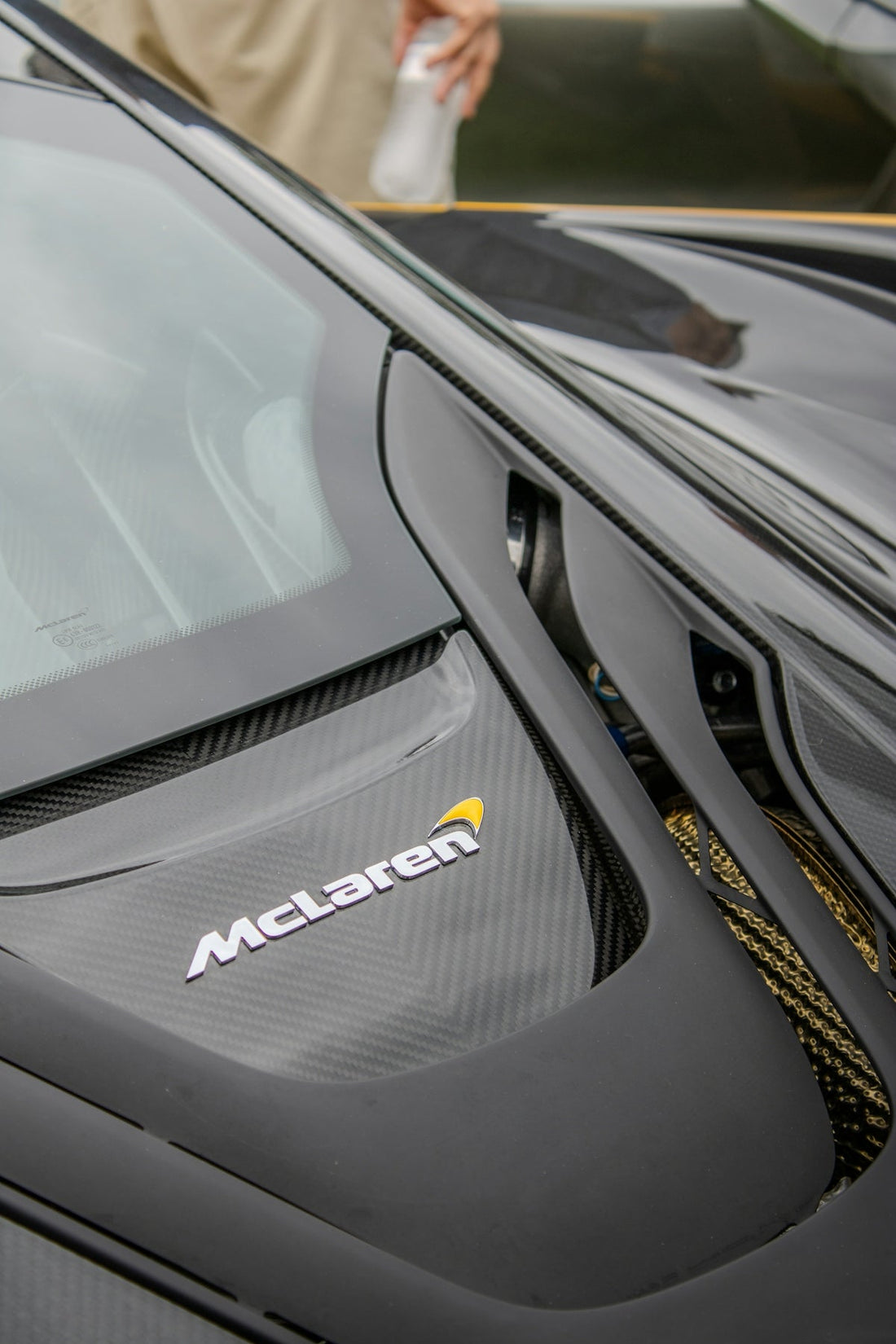 Close-up of McLaren supercar carbon fiber engine cover with logo and gold accents